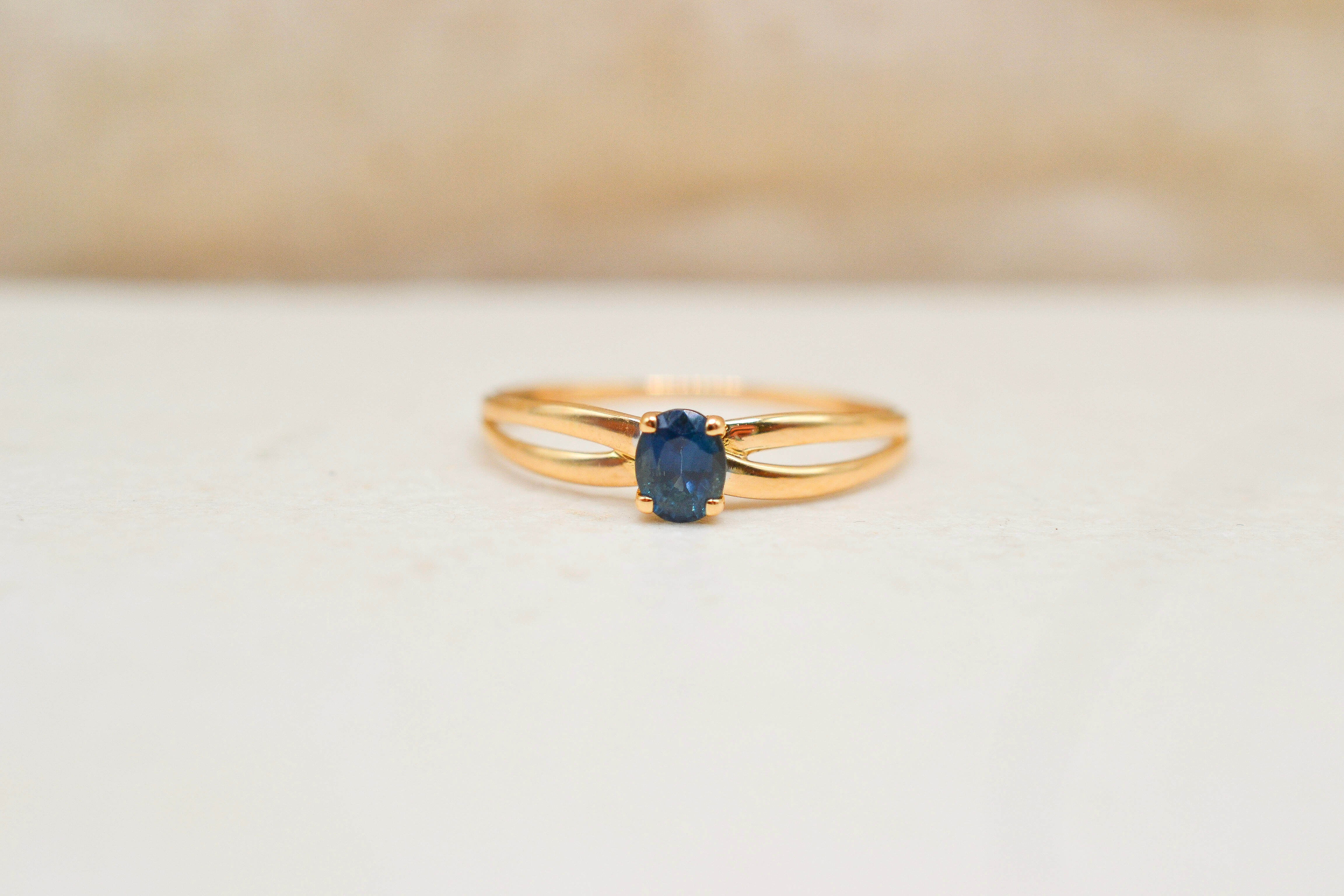 bague en or jaune 18 Carats ornée d'un saphir central, l'anneau se divise en deux branches, ce qui donne l'effet d'un ruban.