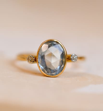 Bague ancienne en Or jaune 18 carats centrée d'une Aigue-Marine sertie clos épaulée par des fleurs d'Or blanc