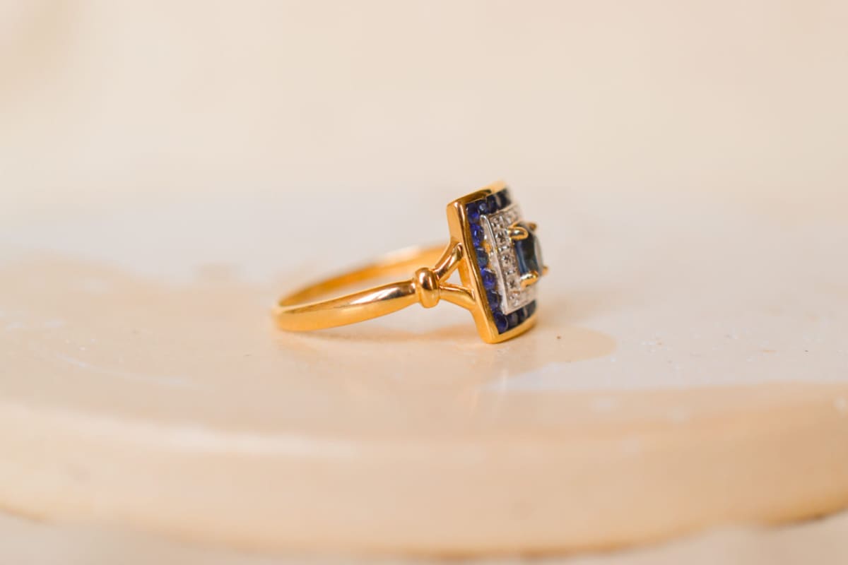 Bague Vintage en Or jaune 18 carats sertie d'un Saphir sur un pavage en Or blanc dans un entourage de Saphirs calibrés
