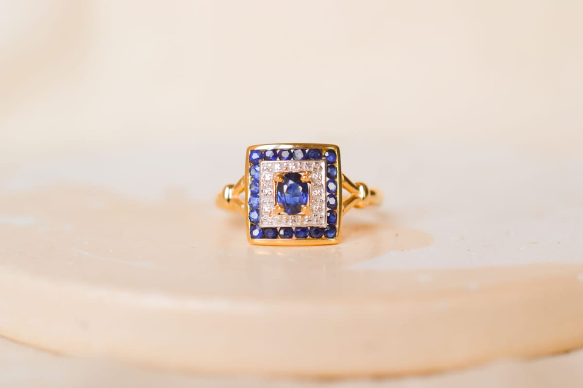 Bague ancienne en Or jaune 18 carats centrée d'un Saphir serti griffes sur un pavage en Or blanc entouré de Saphirs calibrés