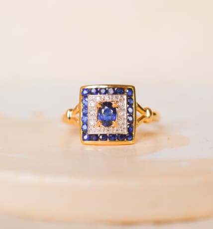 Bague ancienne en Or jaune 18 carats centrée d'un Saphir serti griffes sur un pavage en Or blanc entouré de Saphirs calibrés