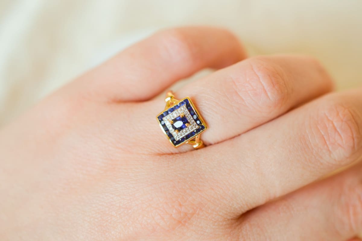 Bague de fiançailles ancienne en Or jaune 18 carats centrée d'un Saphir serti griffes sur un pavage en Or blanc entouré de Saphirs calibrés