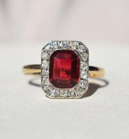 Bague octogonale en or jaune sur le corps de bague et or blanc pour la tête de bague. Tête de bague carrée ornée d'un halo d'oxydes et d'un carré central de verre rouge